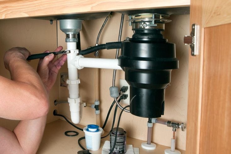 Plumber installing a garbage disposal beneath a kitchen sink in Castle Rock